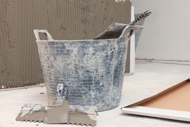 Photo of Bucket near white wall with adhesive mix for tile installation indoors