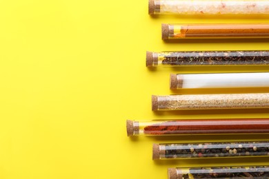 Photo of Glass tubes with different spices on yellow background, flat lay. Space for text