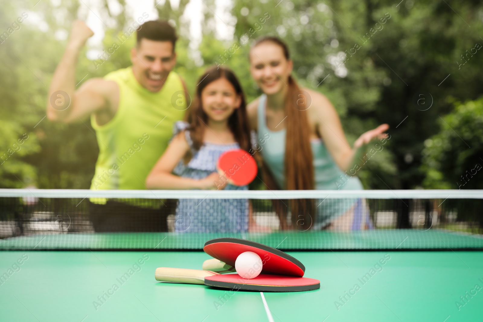 Photo of Family near ping pong table in park, focus on rackets and ball