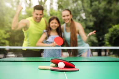 Family near ping pong table in park, focus on rackets and ball