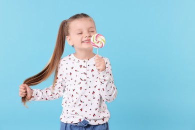 Photo of Happy little girl with colorful lollipop swirl on light blue background, space for text