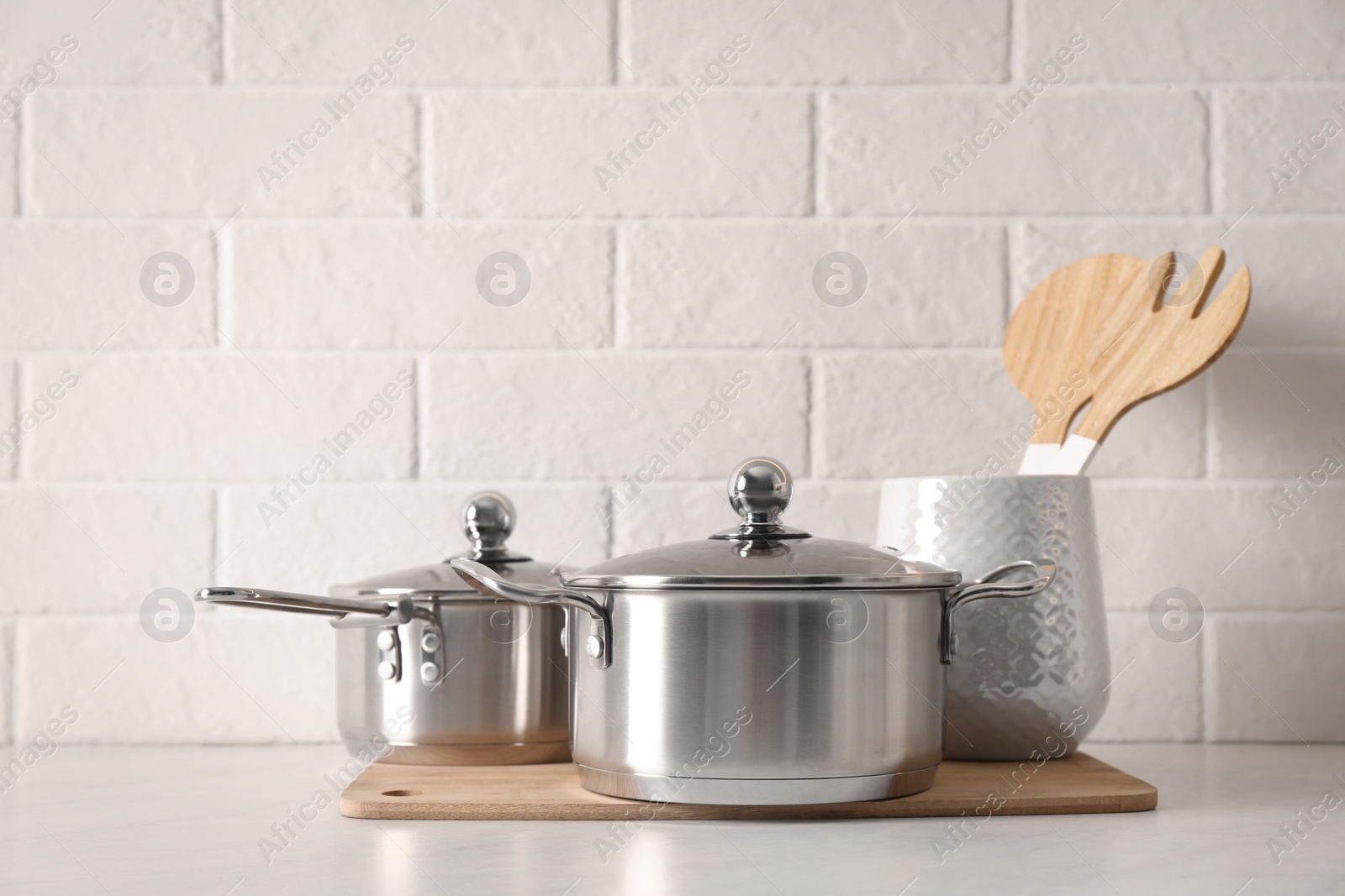 Photo of Pot, saucepan and kitchen utensils on table near white brick wall