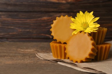 Photo of Natural beeswax cake blocks and flower on wooden table, closeup. Space for text