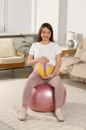 Photo of Beautiful pregnant woman with kinesio tapes doing exercises on fitball at home