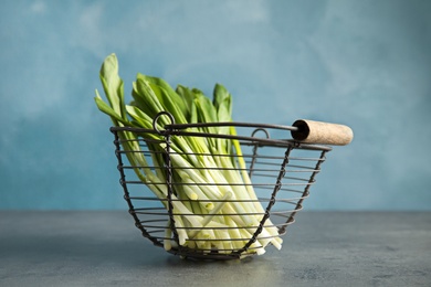 Photo of Basket with wild garlic or ramson on table against color background