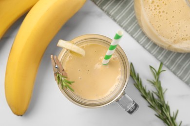 Photo of Mason jar of tasty banana smoothie with straw and fresh fruits on white marble table, flat lay