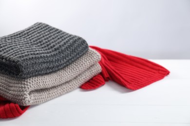 Photo of Stylish knitted scarfs on white wooden table, closeup
