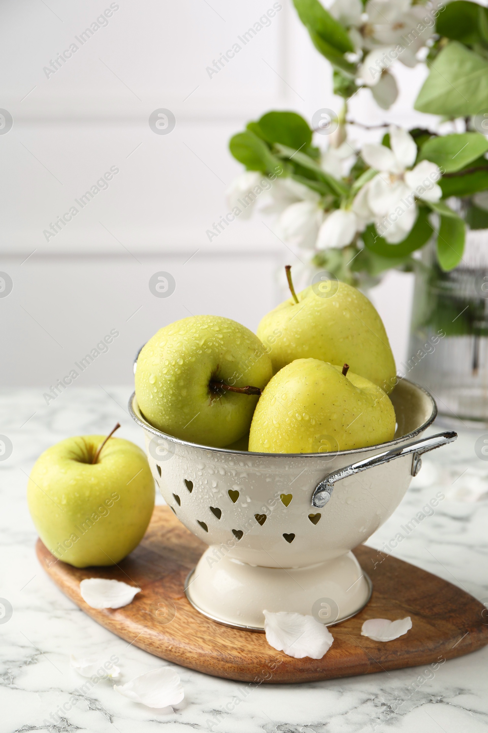 Photo of Colander with fresh apples and flower petals on white marble table