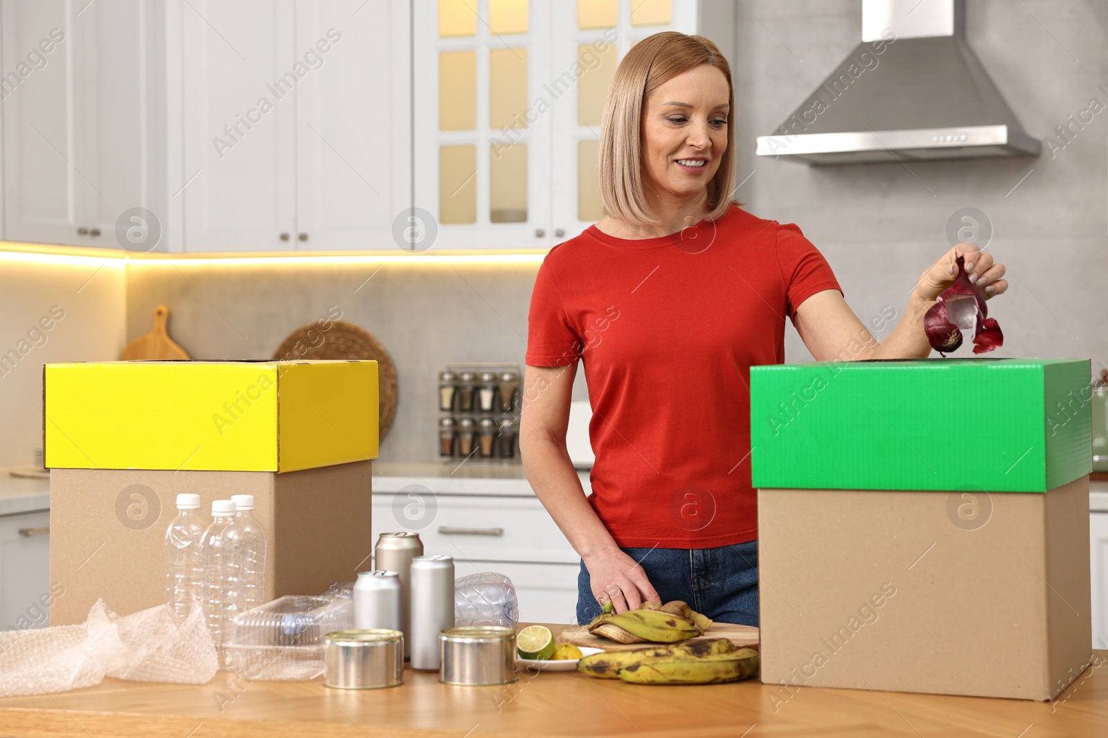 Photo of Smiling woman separating garbage at table in kitchen