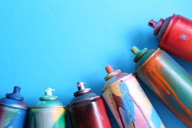 Many spray paint cans on light blue background, flat lay. Space for text
