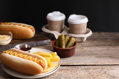 Delicious hot dog with mustard and French fries on wooden table, closeup. Space for text