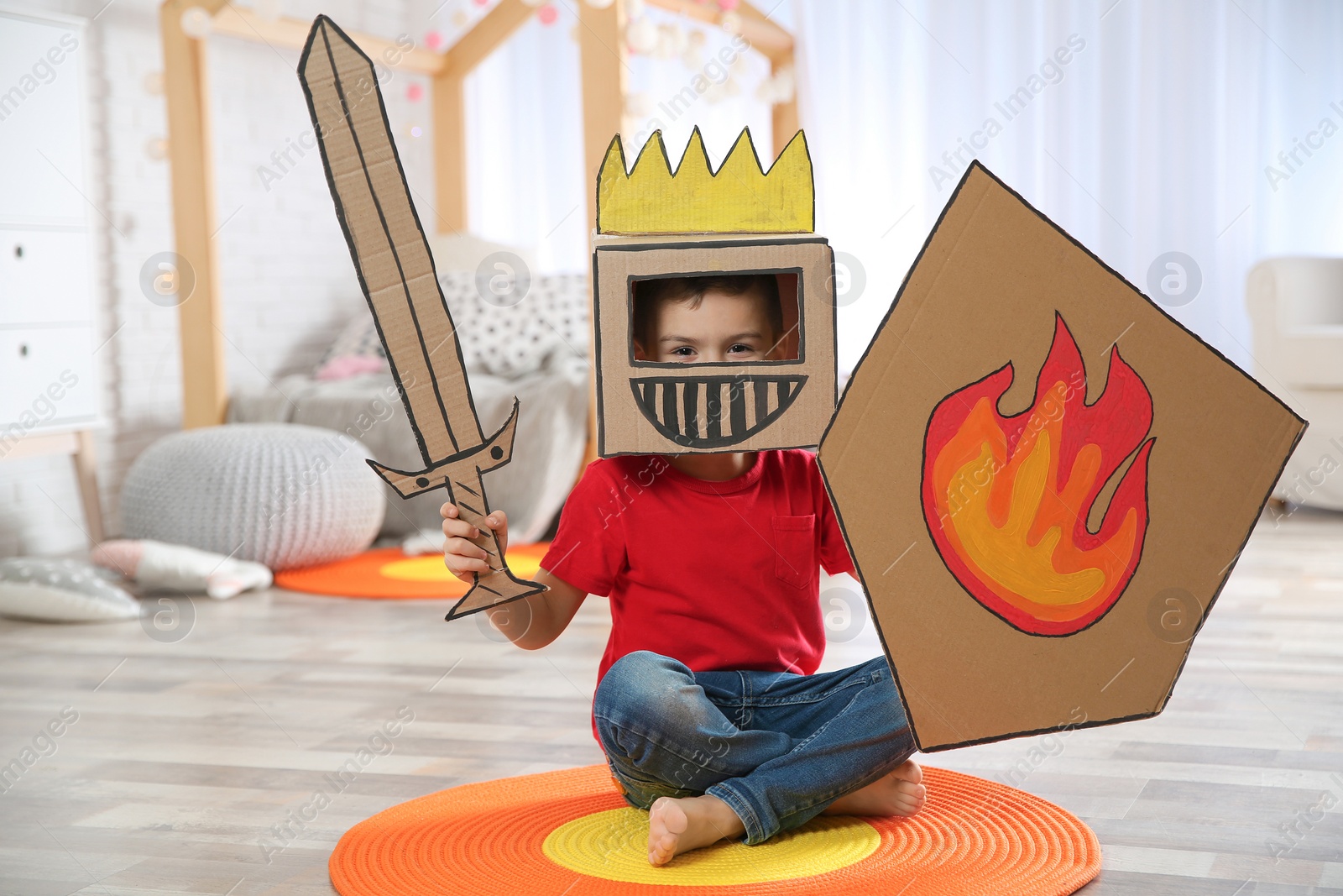 Photo of Cute little boy playing with cardboard armor in bedroom