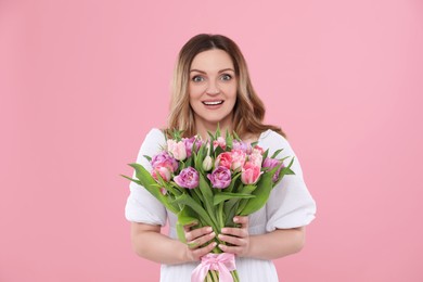 Happy young woman with bouquet of beautiful tulips on pink background