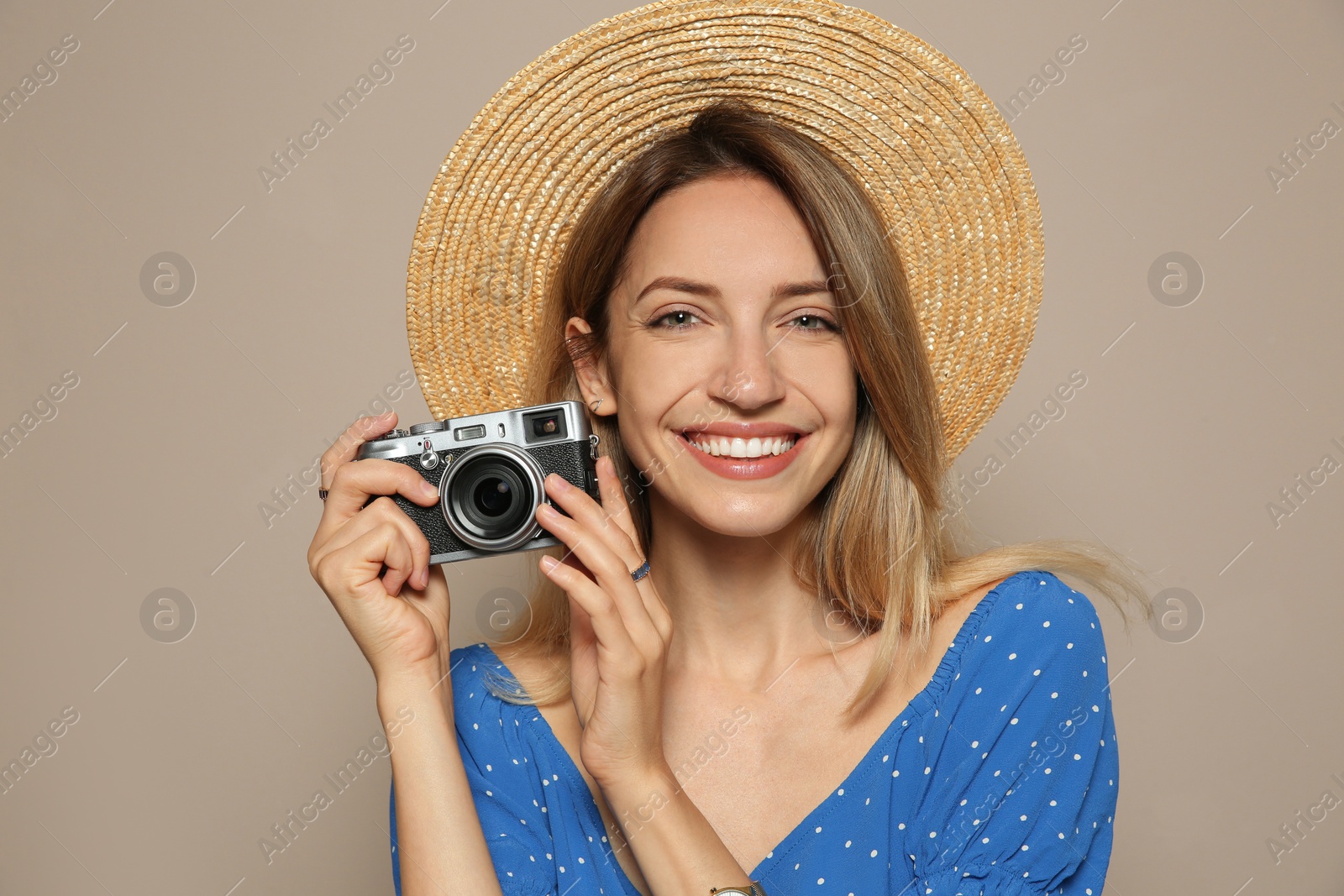 Photo of Beautiful young woman with straw hat and camera on beige background. Stylish headdress