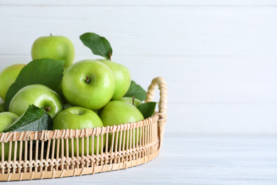 Photo of Juicy green apples in wicker tray on white wooden table, closeup. Space for text