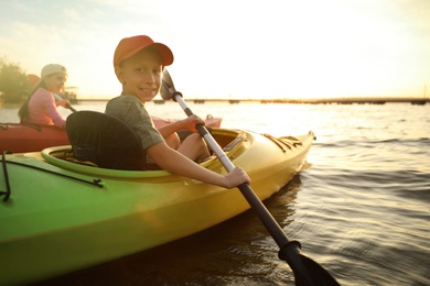 Photo of Happy children kayaking on river at sunset. Summer camp activity