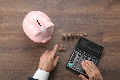 Budget planning. Businessman with piggy bank calculating at wooden table, top view