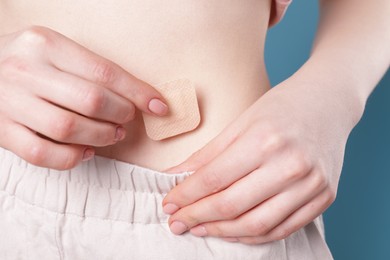 Woman applying contraceptive patch onto her body on blue background, closeup