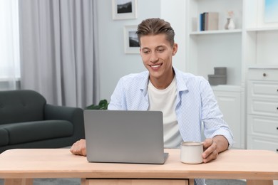 Photo of Happy young man having video chat via laptop at wooden table indoors
