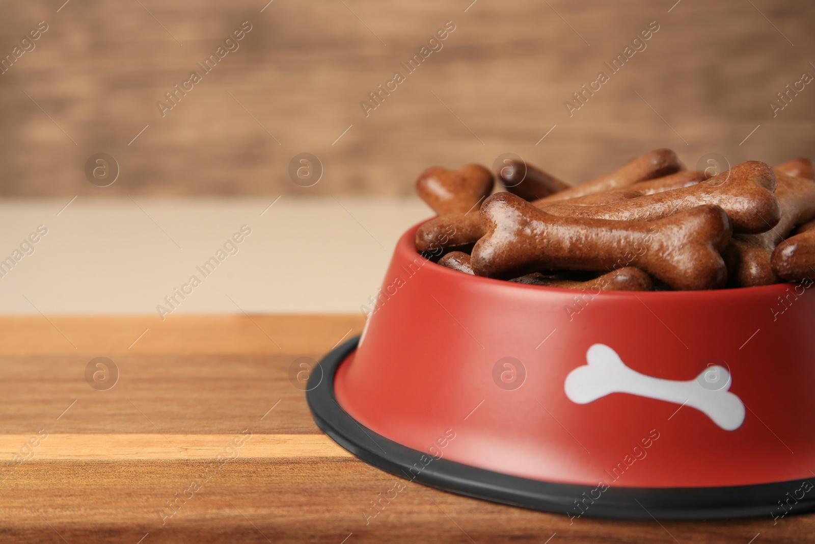 Photo of Red bowl with bone shaped dog cookies on wooden board, closeup. Space for text