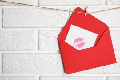 Photo of Red envelope and card with lip print hanging on twine near white brick wall, space for text. Love letter