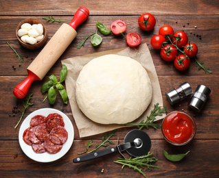 Flat lay composition with dough and fresh ingredients for pepperoni pizza on wooden table