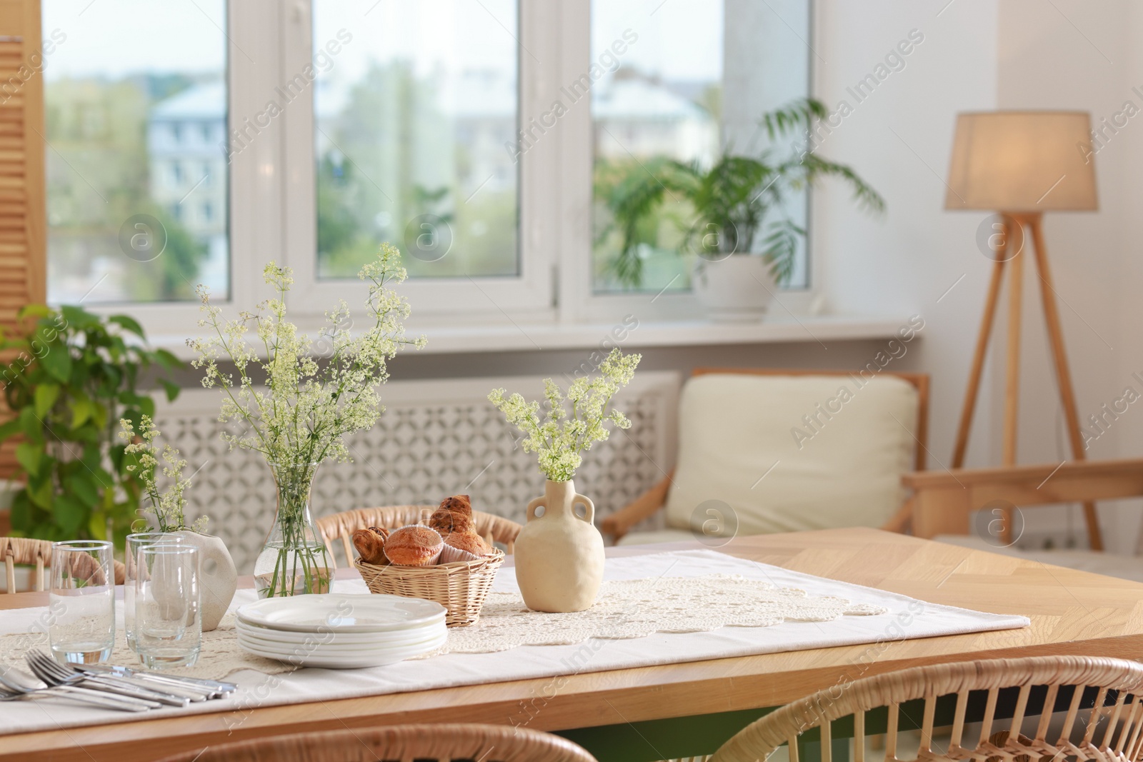 Photo of Clean dishes, flowers and fresh pastries on table in stylish dining room