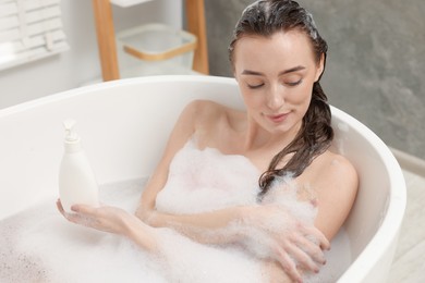 Photo of Woman taking bath with shower gel in bathroom