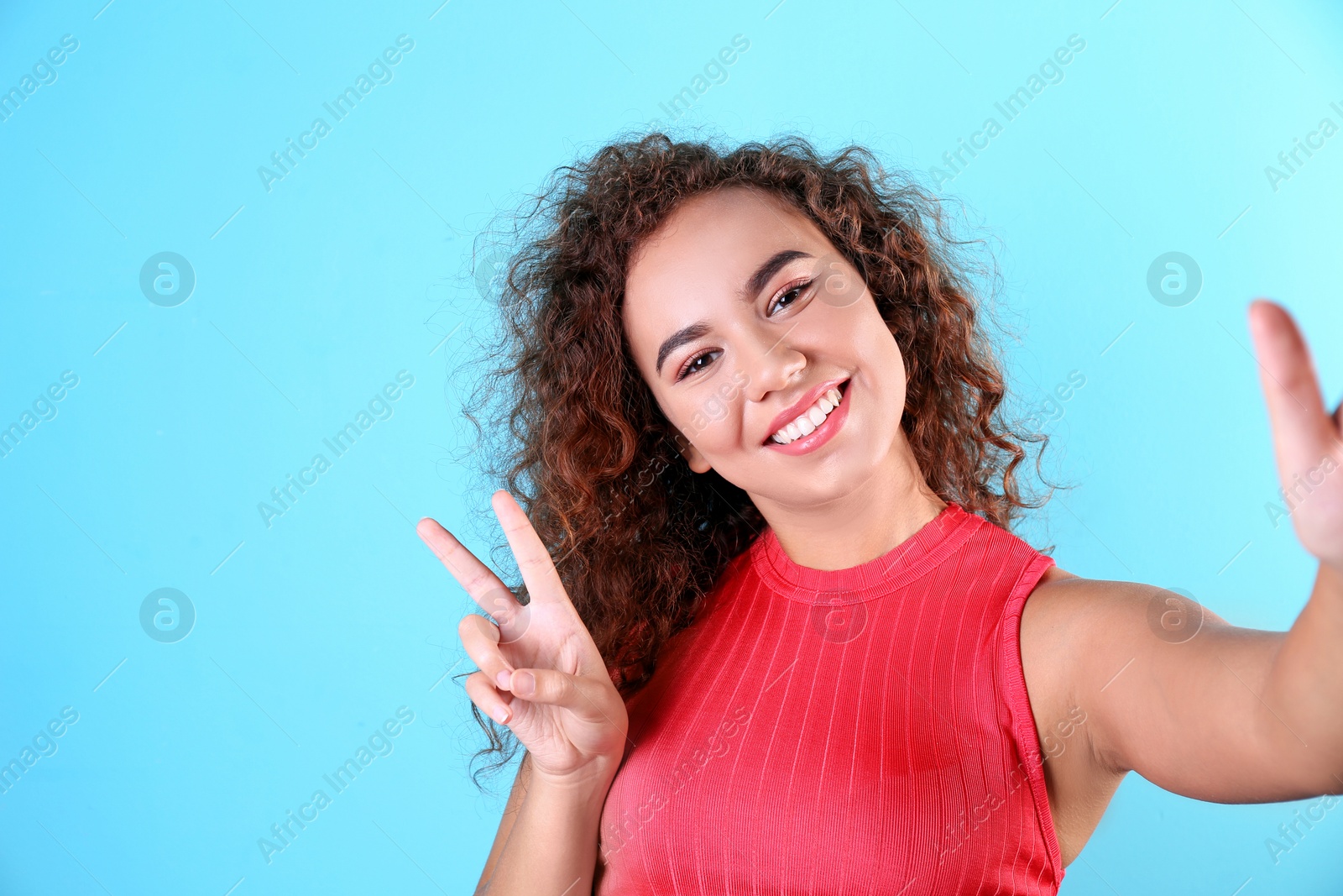 Photo of Young laughing African-American woman taking selfie on color background