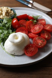 Photo of Delicious burrata cheese with tomatoes and arugula served on wooden table, closeup