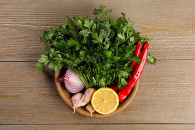 Photo of Bowl with fresh green parsley, chili peppers, lemon, onion and garlic on wooden table, top view