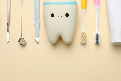 Photo of Tooth model with cute face, oral care products and dental tools on beige background, flat lay. Space for text