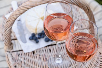 Photo of Glasses of delicious rose wine and food on picnic basket outdoors, closeup