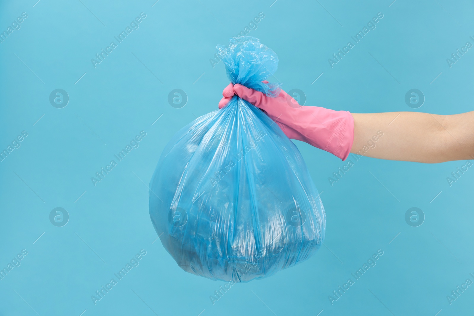 Photo of Woman holding plastic bag full of garbage on light blue background, closeup