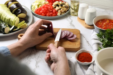 Photo of Cooking delicious ratatouille. Woman cutting fresh onion at white marble table, closeup
