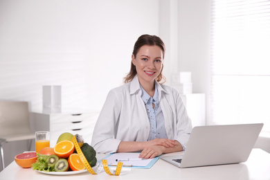 Photo of Nutritionist with clipboard and laptop at desk in office