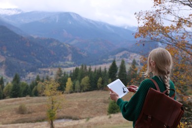 Young woman drawing on tablet in mountains, back view. Space for text