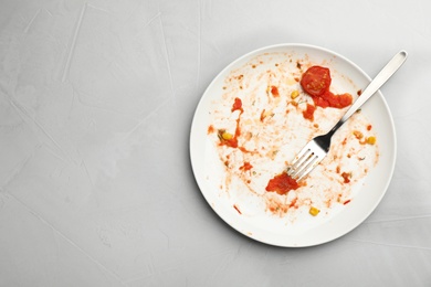 Photo of Dirty plate with food leftovers and fork on grey background, top view. Space for text