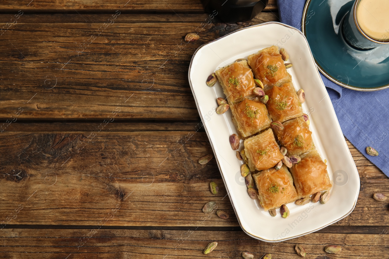 Photo of Delicious baklava with pistachios, hot drink and nuts on wooden table, flat lay. Space for text