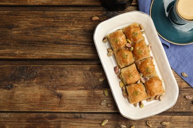 Delicious baklava with pistachios, hot drink and nuts on wooden table, flat lay. Space for text