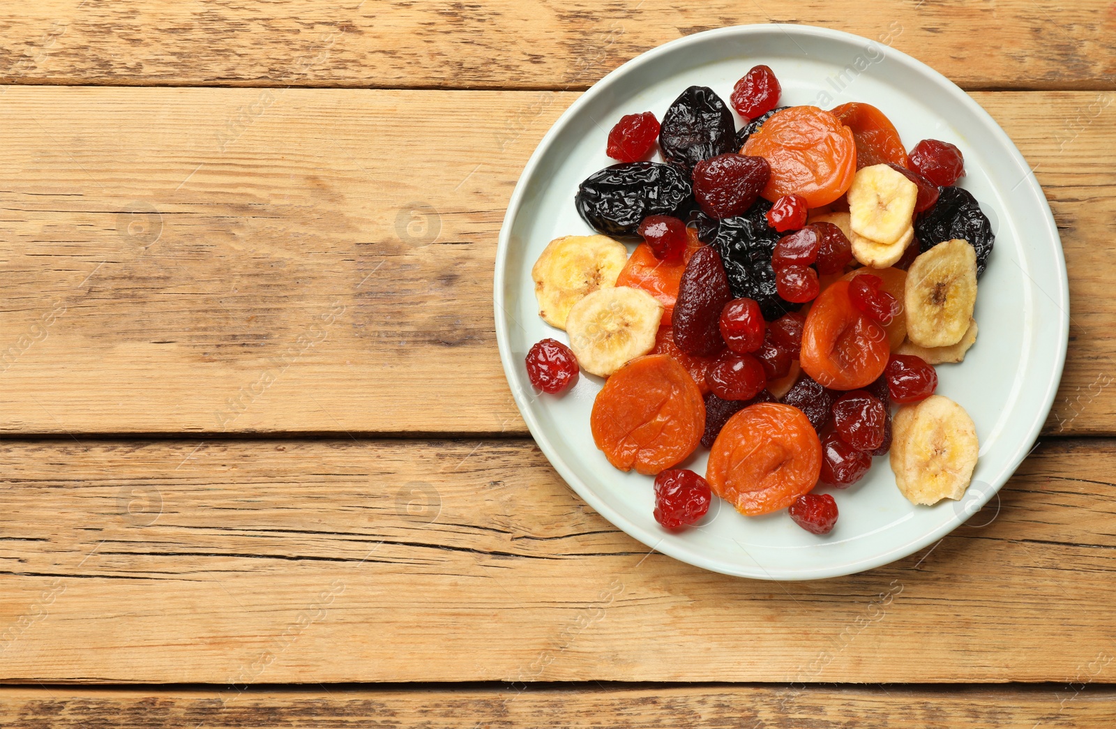 Photo of Mix of delicious dried fruits on wooden table, top view. Space for text