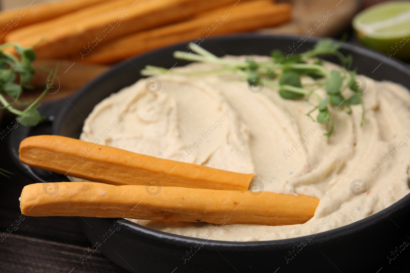 Photo of Delicious hummus with grissini sticks on wooden table, closeup