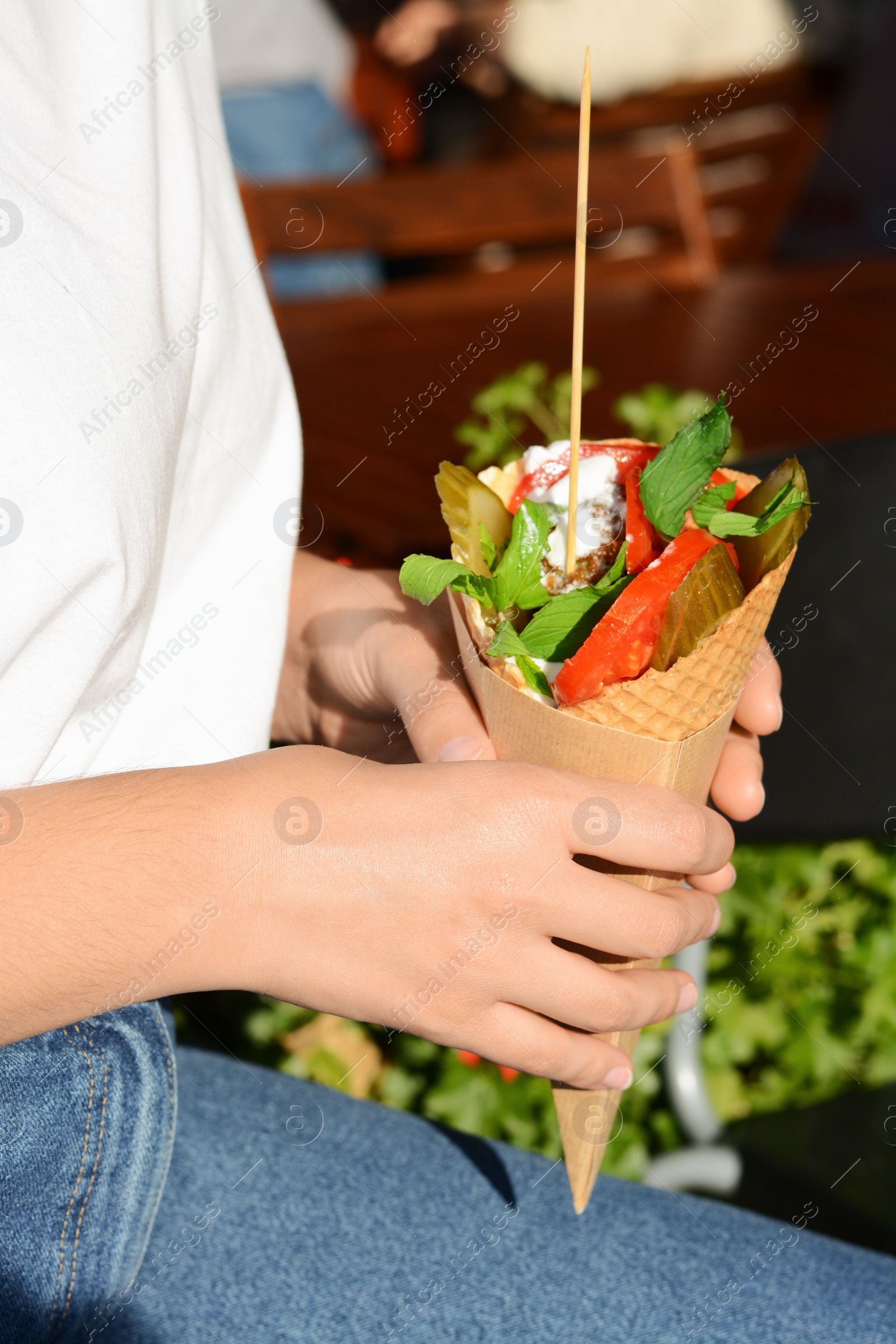 Photo of Woman holding wafer with falafel and vegetables outdoors, closeup. Street food