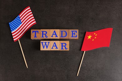 Photo of Words Trade War made of wooden cubes, American and Chinese flags on grey table, flat lay