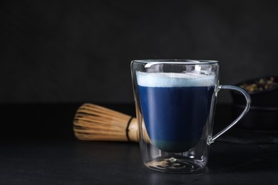 Photo of Delicious blue matcha drink and chasen on black table, space for text