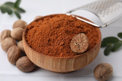 Nutmeg powder in bowl and seeds on white table, closeup