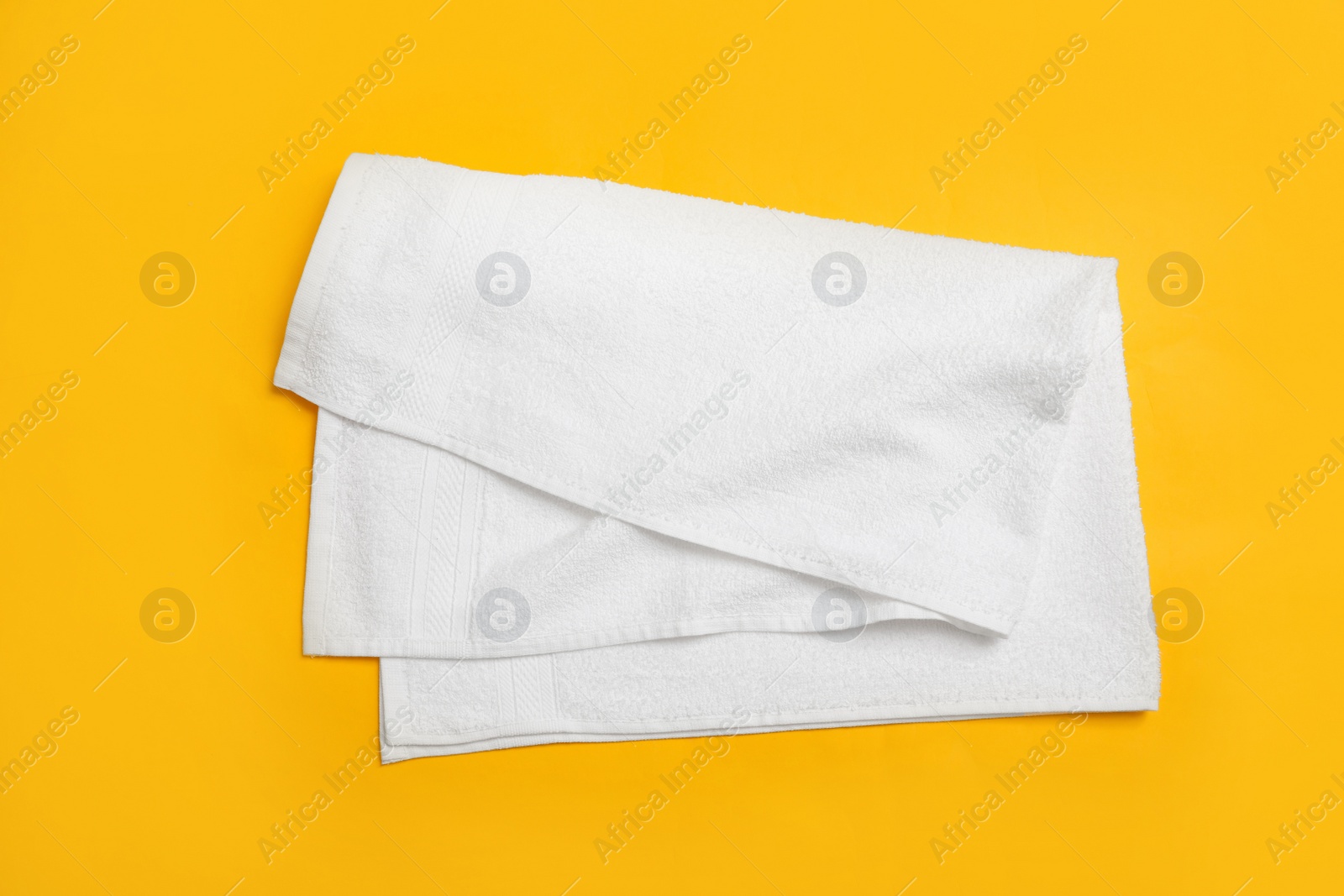 Photo of Folded white beach towel on yellow background, top view