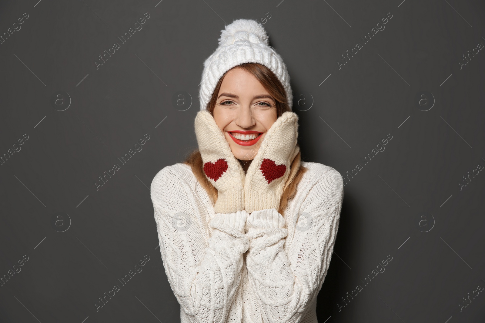 Photo of Beautiful young woman in warm sweater with hat and mittens on dark background