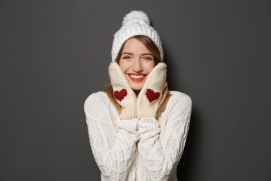 Beautiful young woman in warm sweater with hat and mittens on dark background