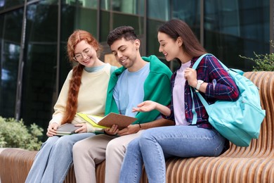 Photo of Happy young students studying with notebooks on bench outdoors